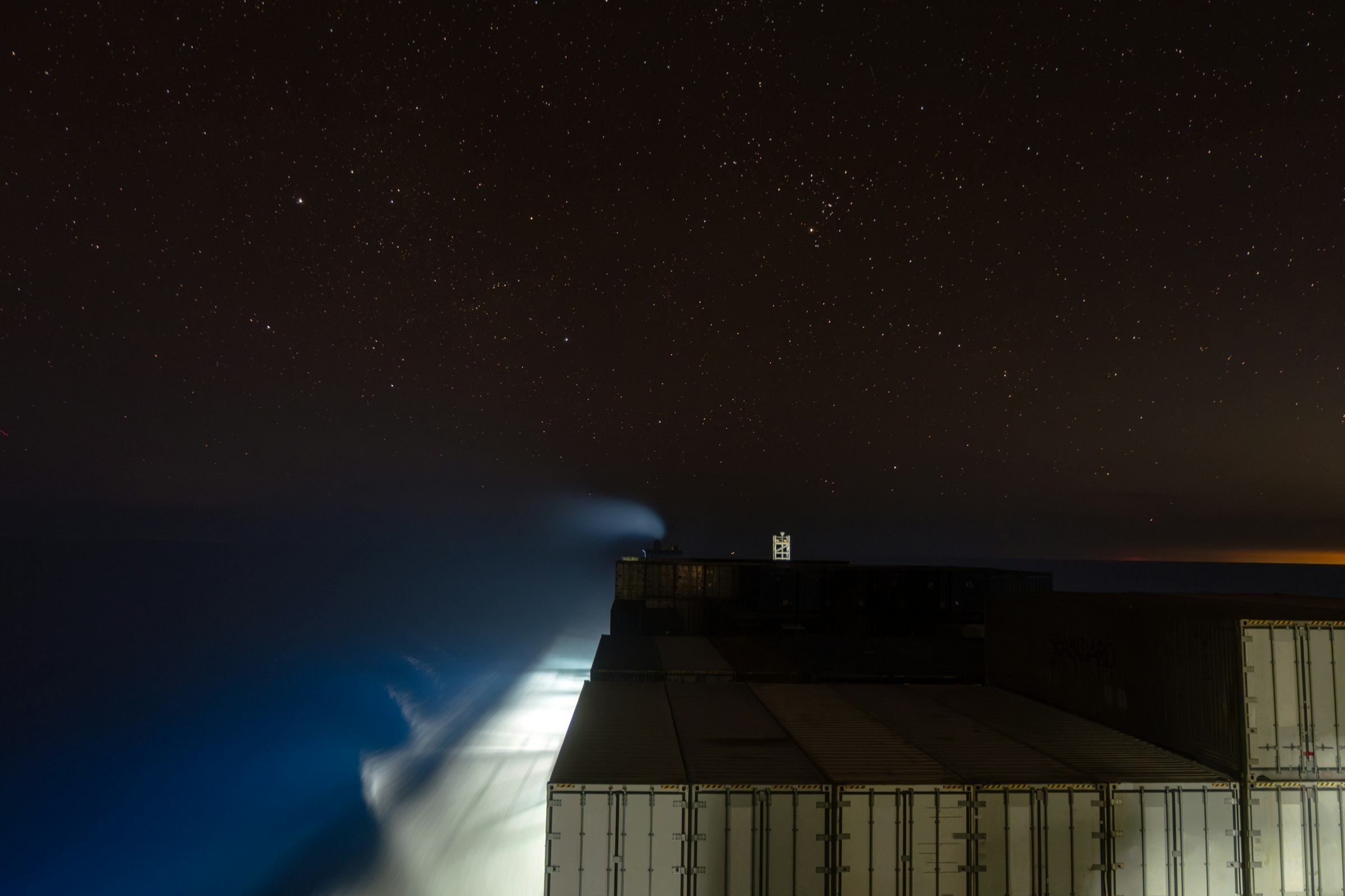 Stacked shipping containers on a vessel under a star-filled night sky