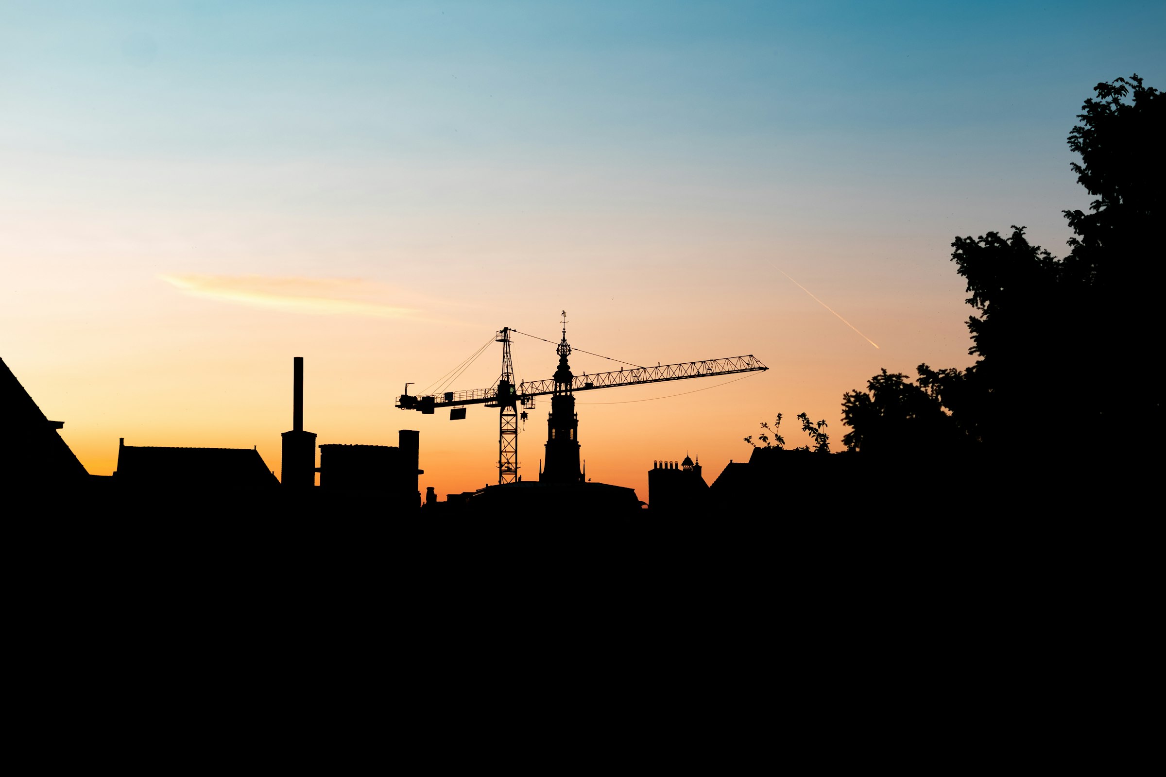 A construction crane silhouetted against a dusk sky above a city skyline