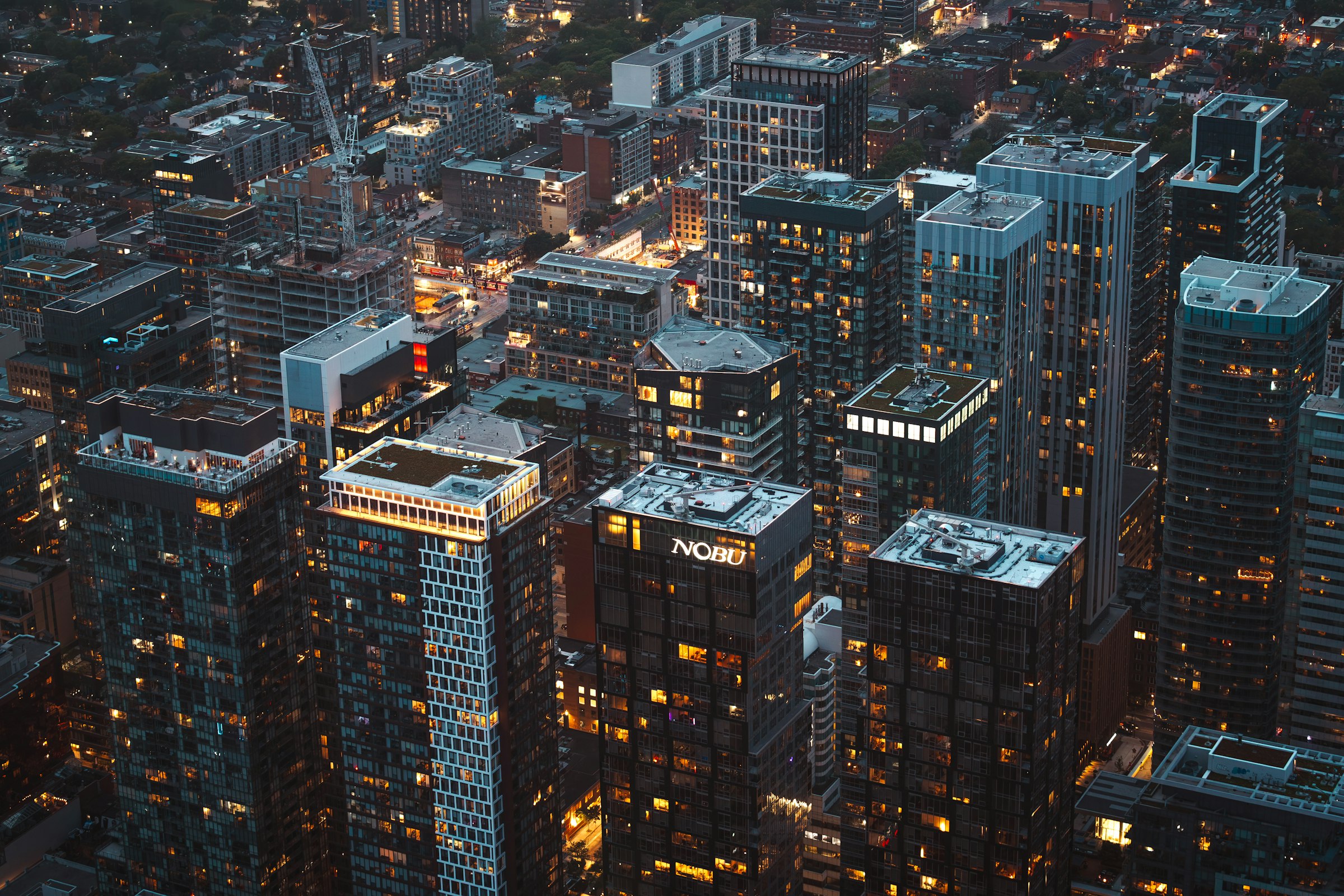 A dense city skyline at dusk, office towers lit from within