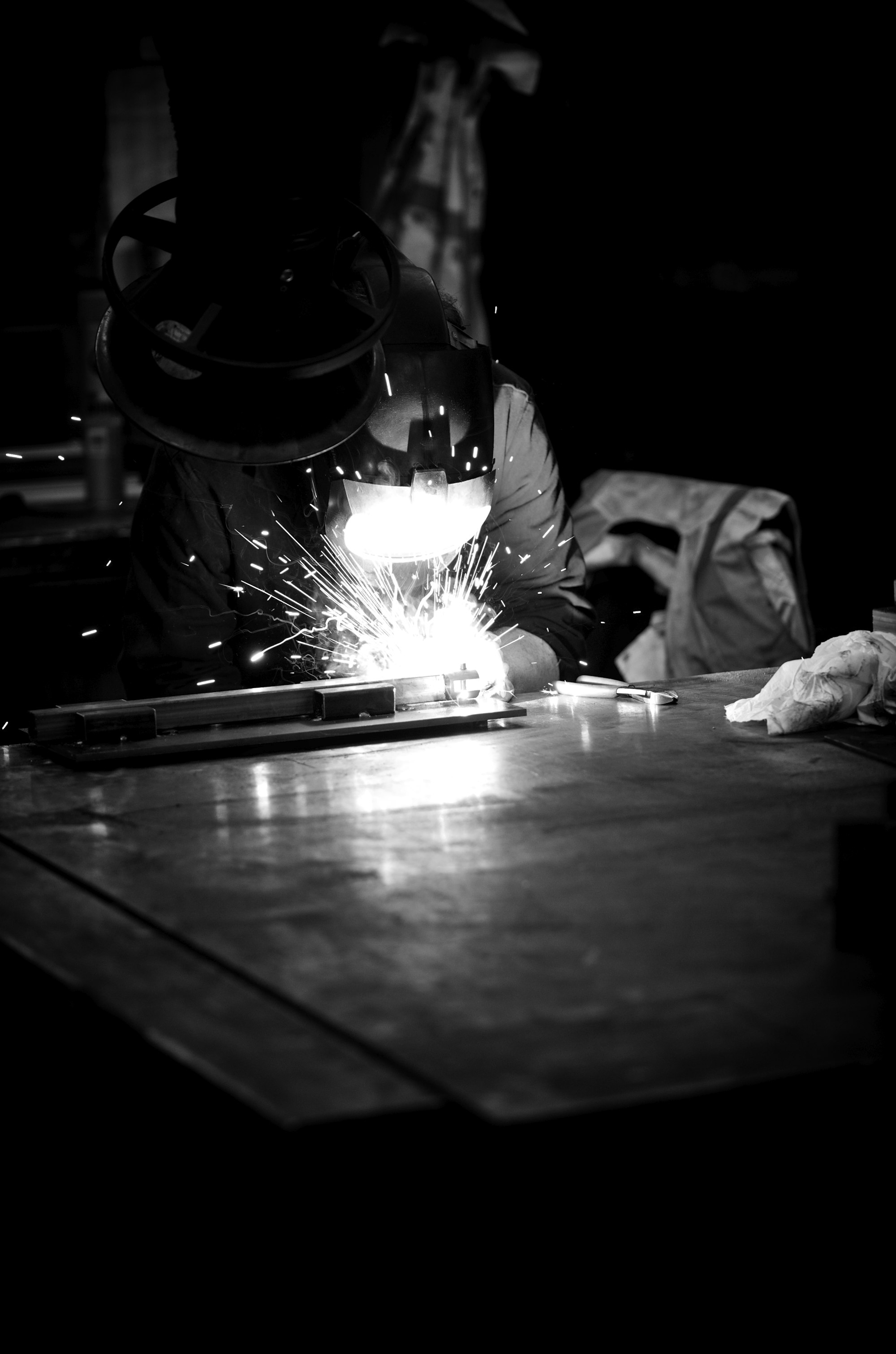 A welder at work, sparks flying, in a dark workshop — skilled people at the centre